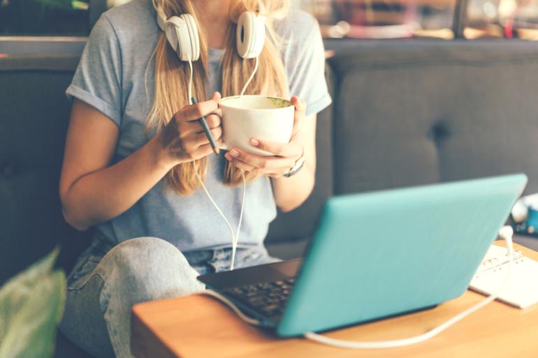 Mujer frente a un computador con un café en la mano 